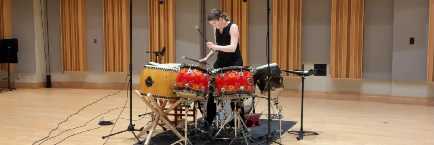 Liz Morad playing a set of red and gold drums in a recital hall